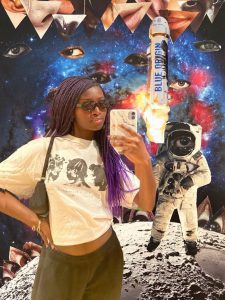 A photo collage of a young black woman taking a selfie in front of an astronaut and space. Collaged onto the space are eyes and mouths cut from a magazine.