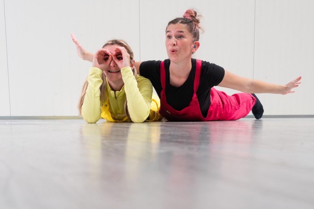Photo of two young white women lying on their fronts, in playful poses.