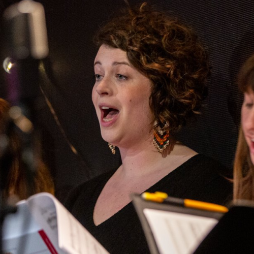 Cathy Phillips Brady, a girl with curly brown hair singing with a folder at BBC Radio Theatre in December 2022