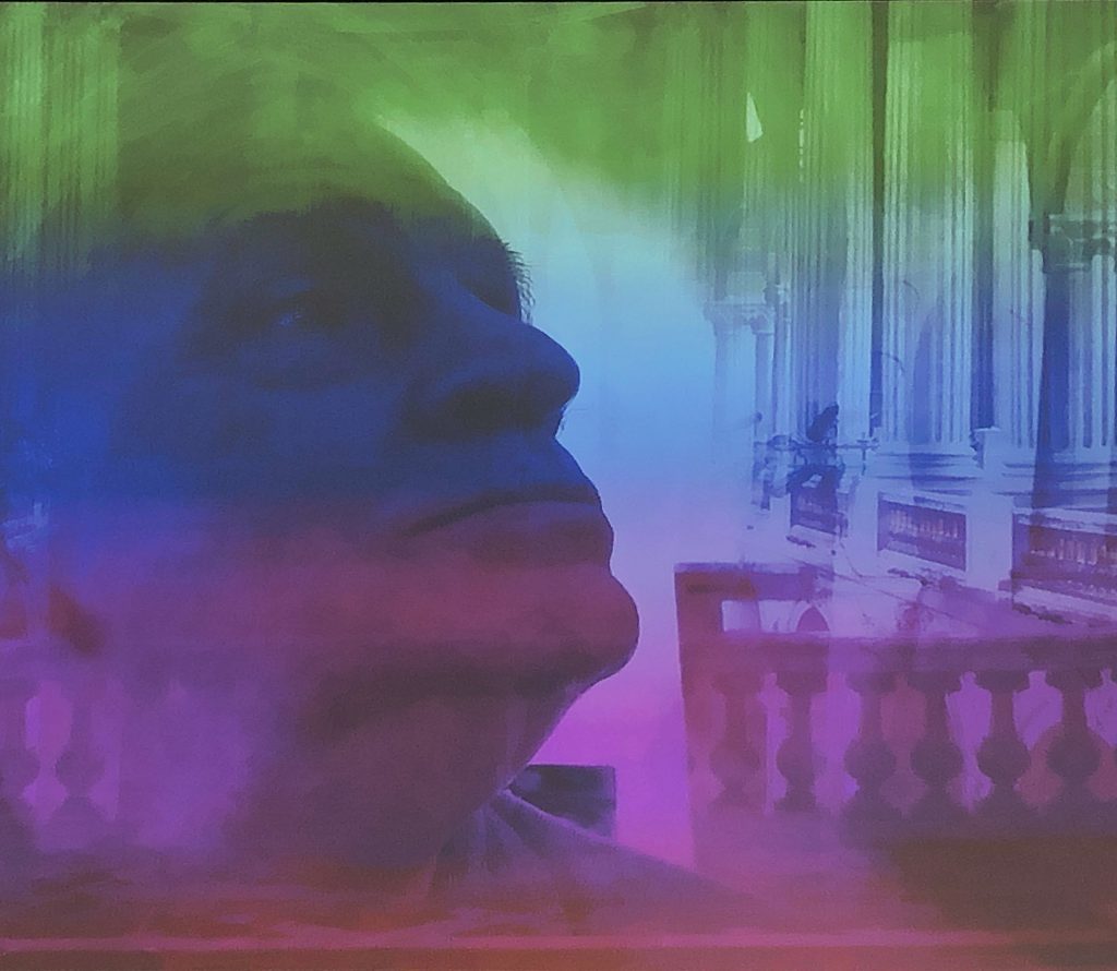 A man's face with layers of a building behind and differently coloured filters over.