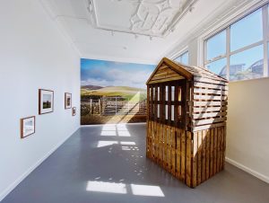 Gallery installation showing a wooden crate that features a sound installation. A large vinyl on the wall. Three framed images.
