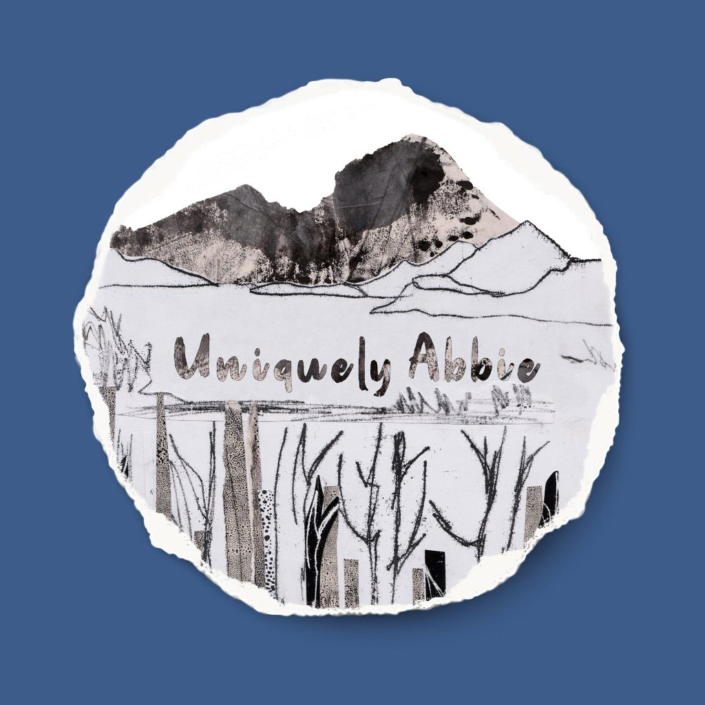 A highlands landscape made of monoprint and collage sits inside a circle with a blue backround. The words uniquely abbie written in the same style of as the collage paper.