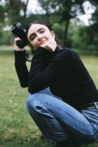A white woman with dark hair, crouching down and holding a camera.