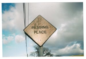 A 4x6 inch printed photograph from 35mm film of a passing place, a diamond-shaped white sign with the words PASSING PLACE. The sky is cloudy and there is a phone line going overhead.