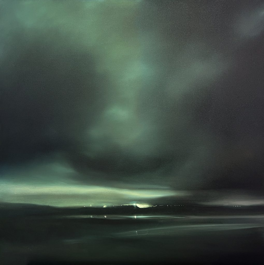 Dark green night skies over a sea and beach lit up by city lights in the distance and a lighthouse closer by