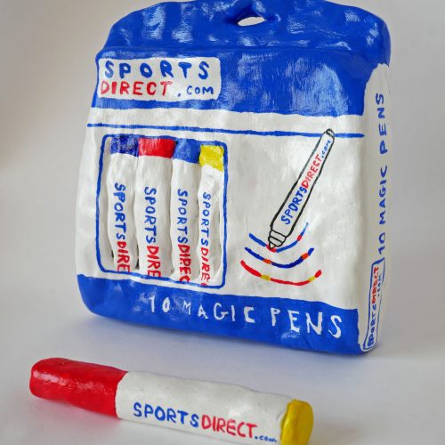 A clay model, decorated in acrylic paint and glazed, of a bag of Sports Direct branded pens with one model lying in front of the bag.