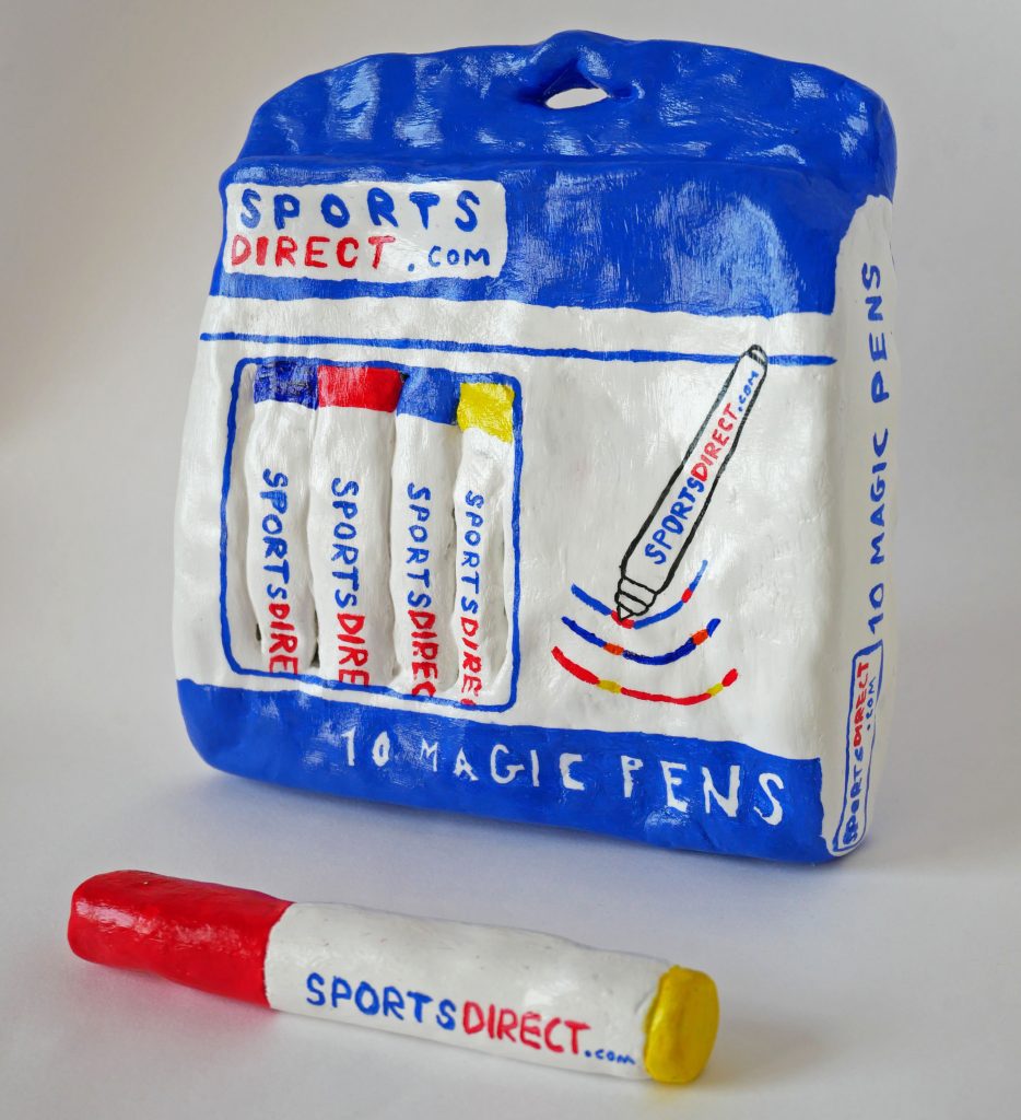A clay model, decorated in acrylic paint and glazed, of a bag of Sports Direct branded pens with one model lying in front of the bag.