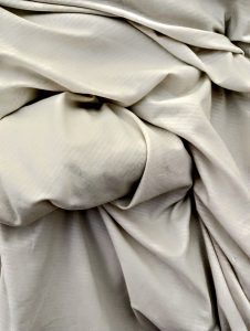 A cream piece of fabric which has lots of folds in it, with high contrast revealing the shadows and depth in each fold.