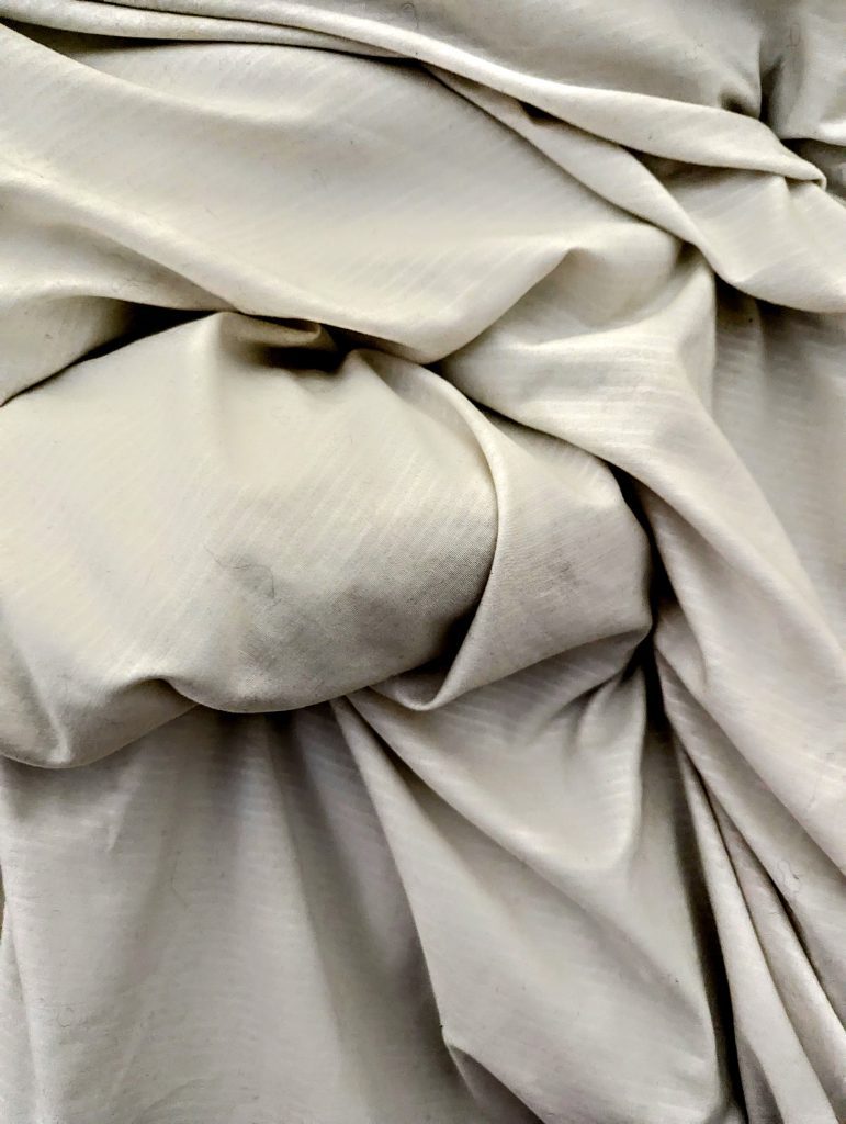 A cream piece of fabric which has lots of folds in it, with high contrast revealing the shadows and depth in each fold.