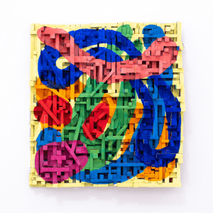 A colourful visual art piece that is wall-mounted. The work is made from small rectangular boxes made of paper prints. On top of this complex shape of small boxes, it has been painted in bright, colourful, undulating shapes.
