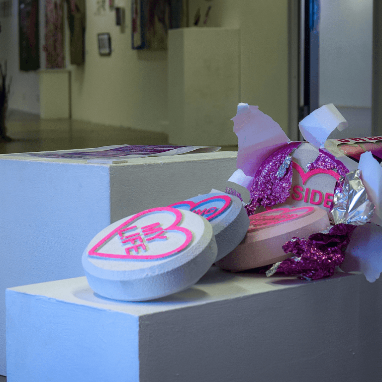 Sculpture of enlarged love heart sweets with custom quotes on pink foil.