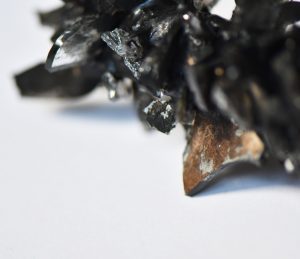 A very close up image shows a black wax crayon with shards of broken reflective glass sticking out.