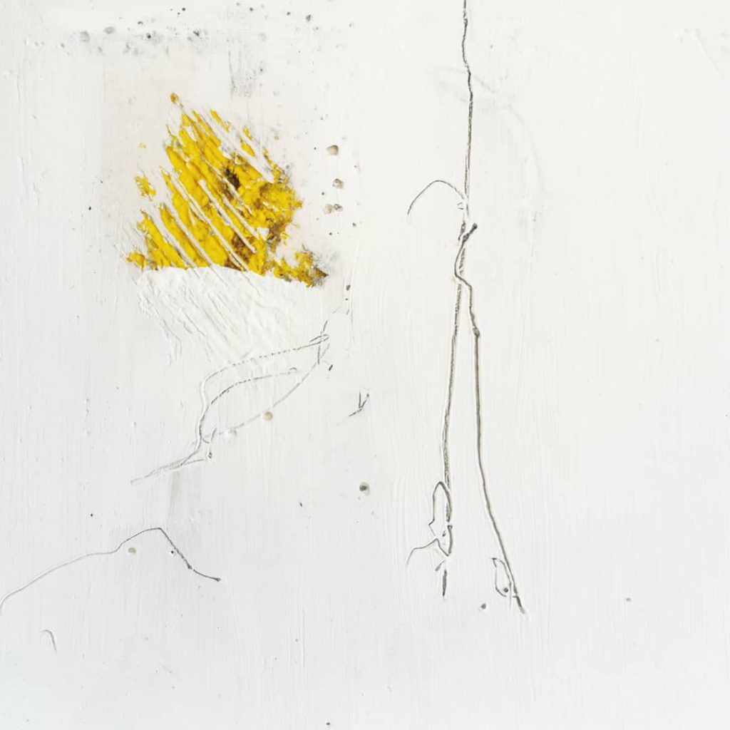 A small square made of concrete and plaster with some marks made on it, it is mostly white but there is some yellow coming though from underneath at one part.