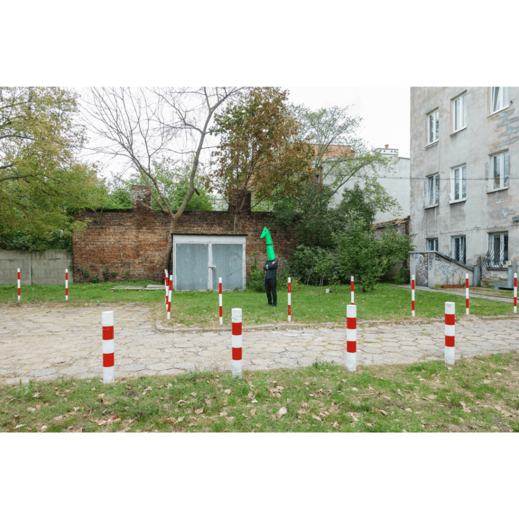 The artist, dressed up as a green-headed monster, standing in the middle of an urban setting in Poland.