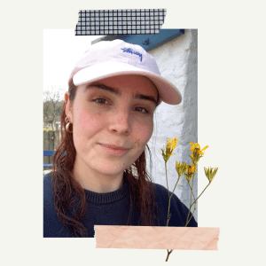 A white woman with dark hair wearing a pink cap and a navy jumper.