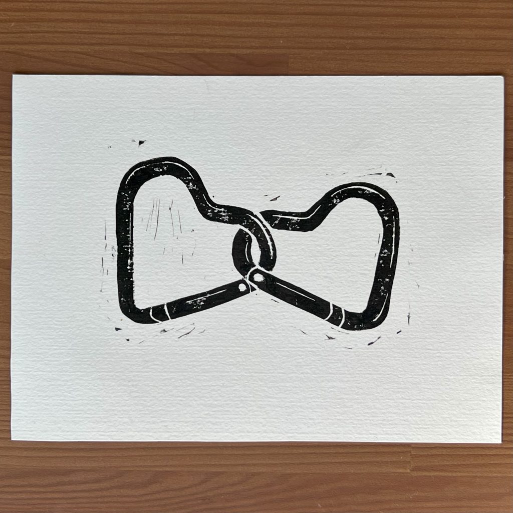 A black ink lino print of two interlocked, heart shaped carabiners.