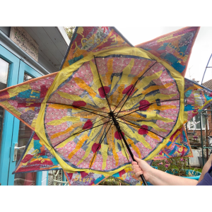 Photo of the inside of a brightly-coloured embroidered umbrella. There is a sun in the centre and rays of light shining outwards. There is embroidered text with words such as relief, powerful, gratitude and reassurance.