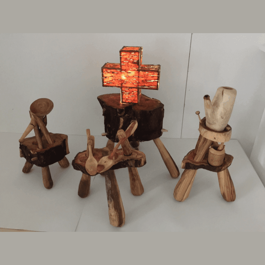 Four small, hand carved wooden sculptures arranged on a plinth. One of them has a glowing orange cross on it.