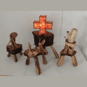 Four small, hand carved wooden sculptures arranged on a plinth. One of them has a glowing orange cross on it.