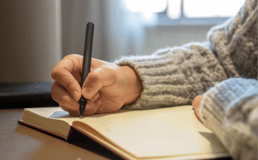 stock image of a person writing longhand in a book. It is a close-up of their hand and arm.