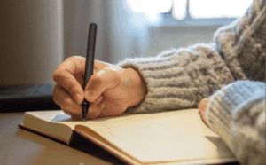 stock image of a person writing longhand in a book. It is a close-up of their hand and arm.