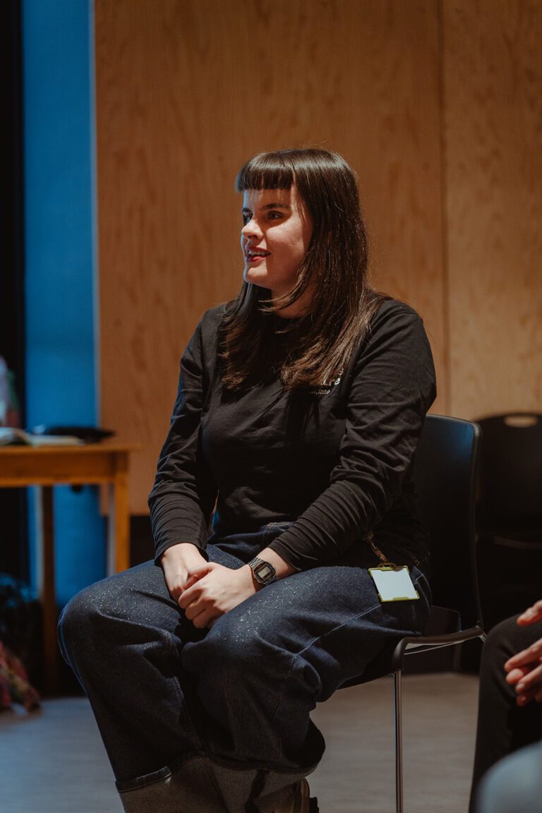 Dark hair female presenting person sitting down delivering a workshop.