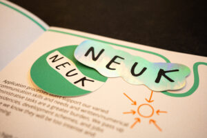 Two stickers that say "Neuk", on top of a copy of the Neuk Manifesto