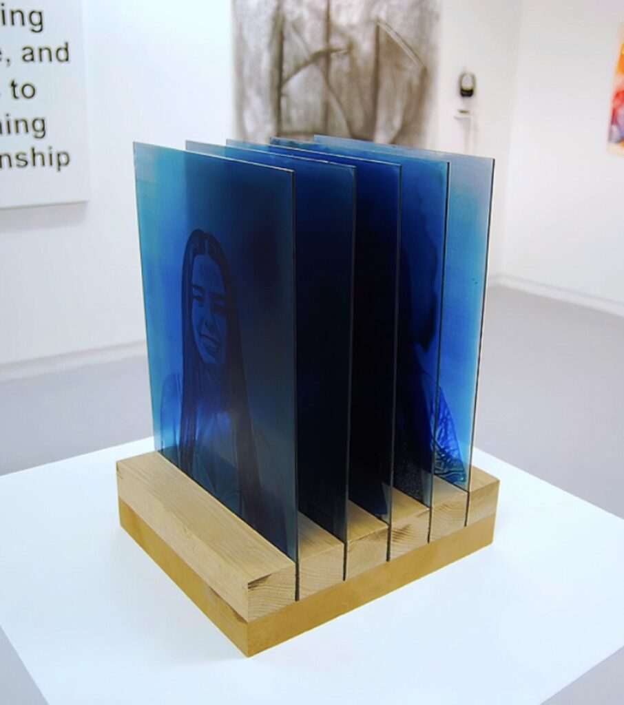 Cyanotype prints on 5 planes of glass, in a row, depicting different emotions and the process of masking on a wooden stand.