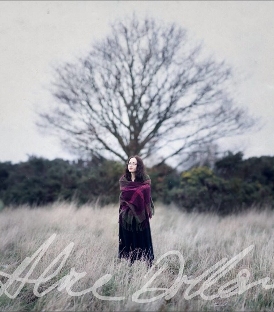 Album art for On a Green Growing Tree. It is a photograph (taken by photographer Aliza Razell) of Alice Dillon, young and with long dark hair, wrapped in a shawl and standing in front of a tree on a wintry day. The text at the bottom reads 'Alice Dillon' in the musician's handwriting.