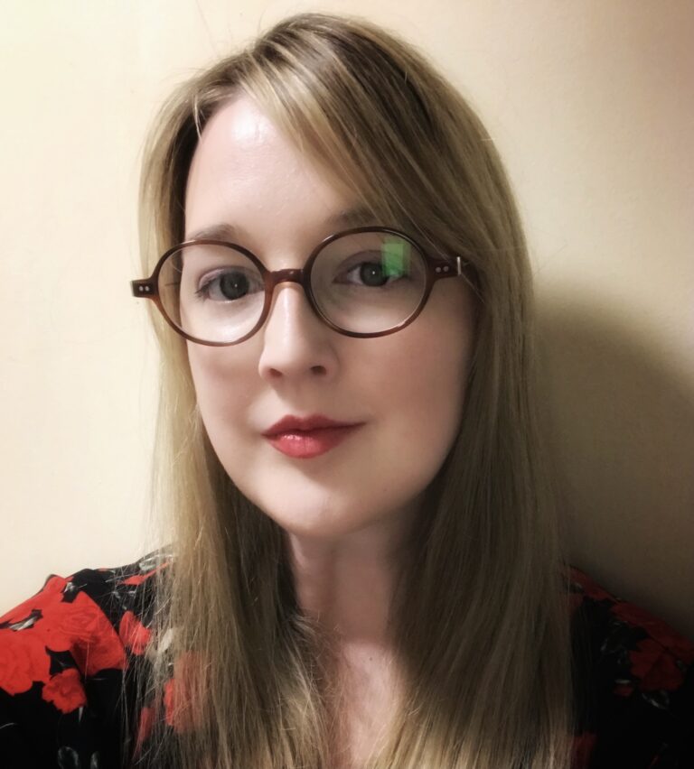 A portrait photo of a female with long blond hair wearing dark framed round glasses.