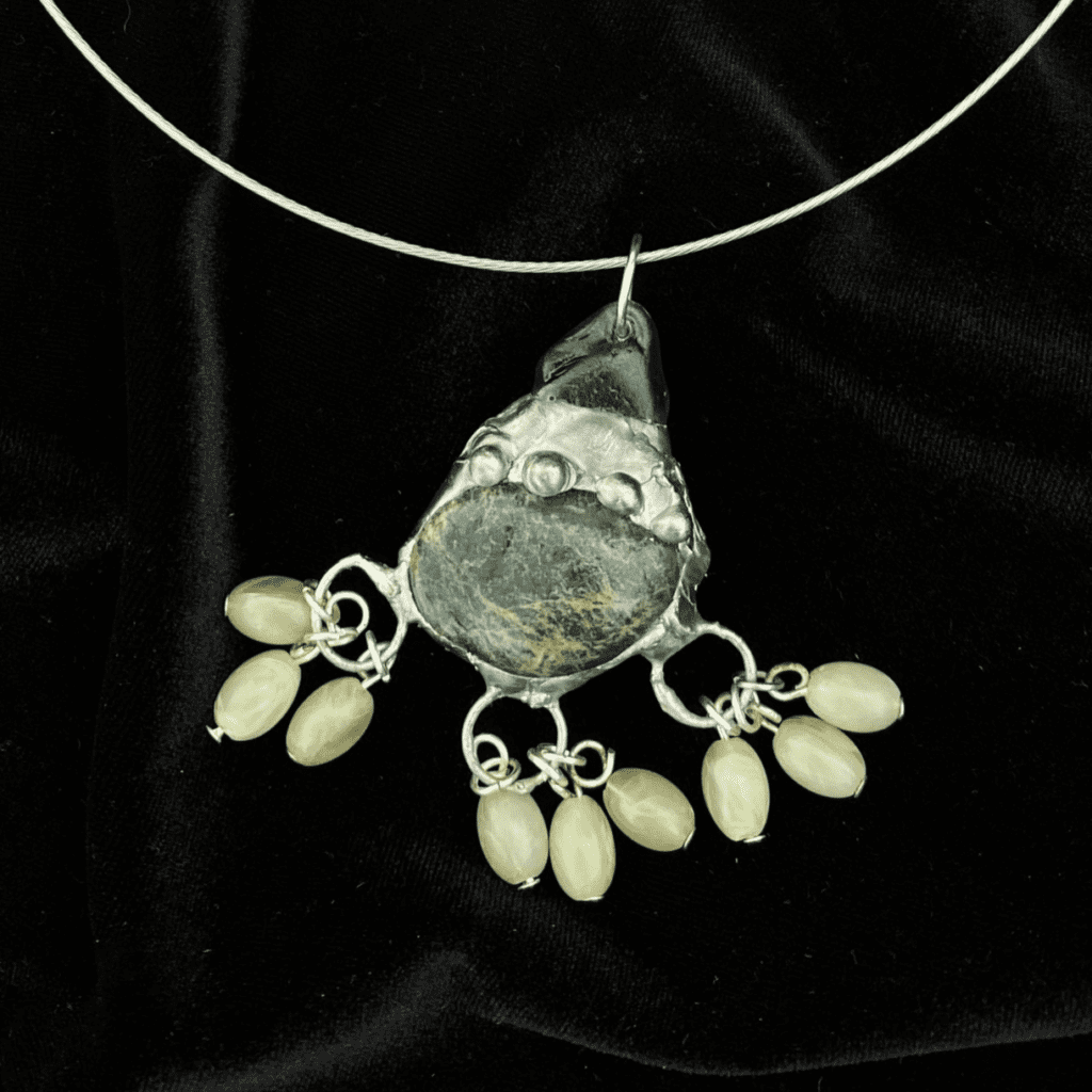 with soldered detailing and three dots on the metal. it is attached to green seaglass and has three sets of three small green beads at the bottom.