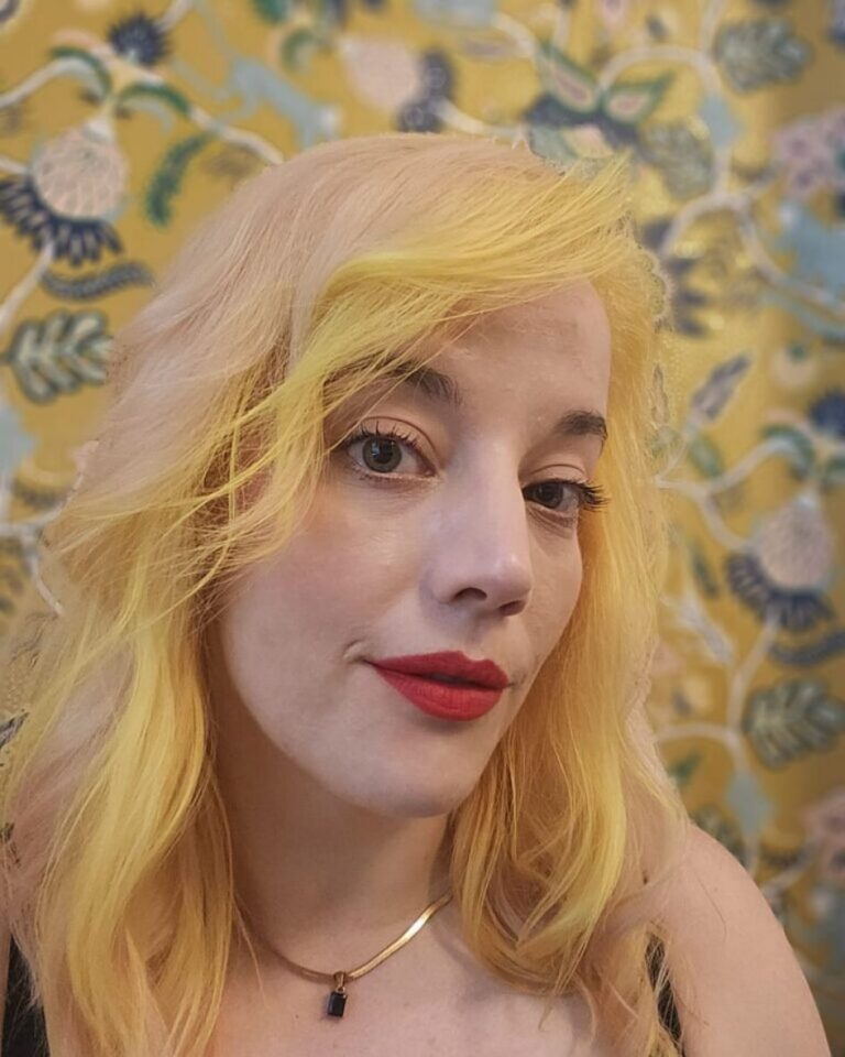 A young white woman with bleached blond hair and red lipstick.