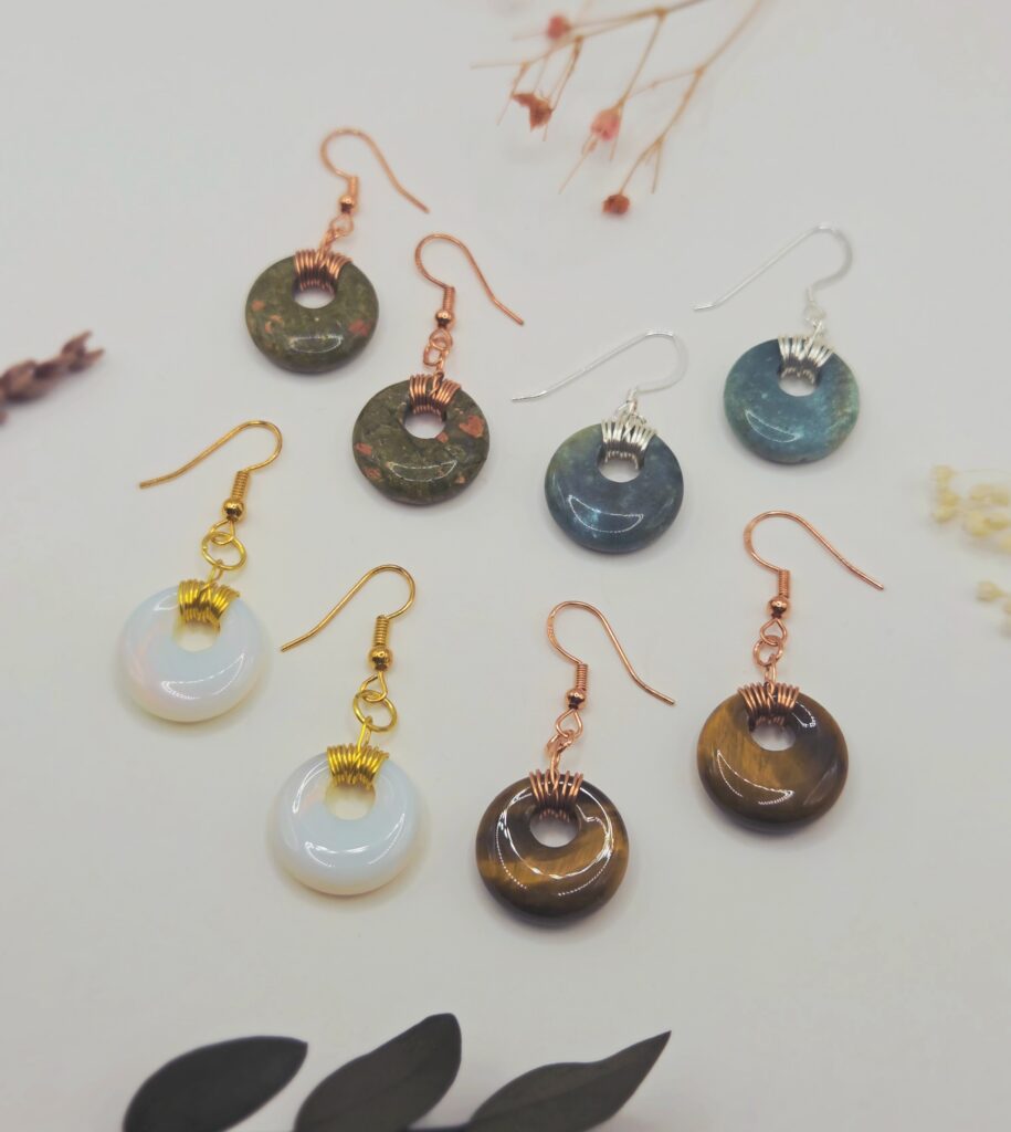 A set of four pairs of dangle earrings, featuring donut-shaped gemstone beads wire-wrapped in various colours of wire. On a white background.