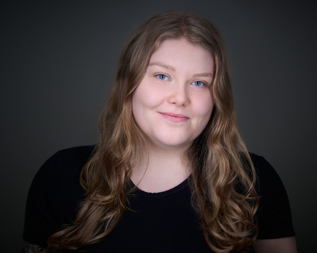 Headshot of Sarah Docherty, who has long brown hair and is wearing a black top.