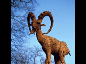 Photograph of a bronze goat statue, against a blue sky