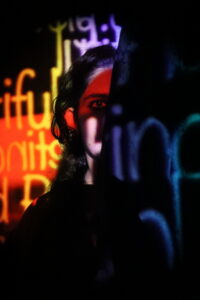 A woman’s face, half covered in black with distorted words written in different colours.