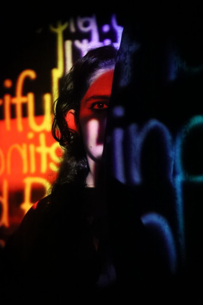 A woman’s face, half covered in black with distorted words written in different colours.
